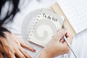 Woman hand writing words to do list on notepad with calendar, goal, and planning concept