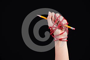 Woman hand with yellow pencil tied with red rope, depicting the idea of freedom of the press or expression on dark background.