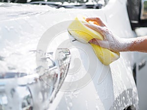 Woman hand with yellow sponge washing car