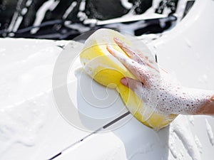 Woman hand with yellow sponge washing car