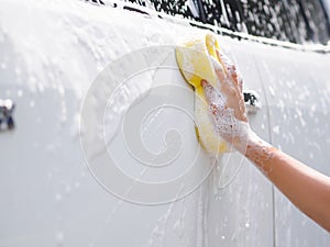 Woman hand with yellow sponge washing car