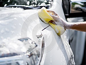 Woman hand with yellow sponge washing car