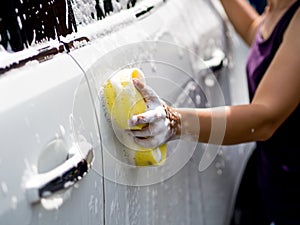 Woman hand with yellow sponge washing car