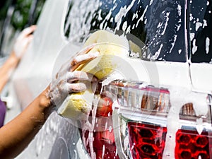 Woman hand with yellow sponge washing car