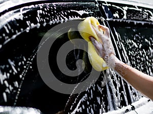 Woman hand with yellow sponge washing car