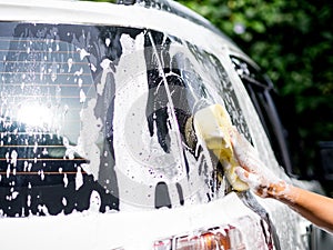 Woman hand with yellow sponge washing car