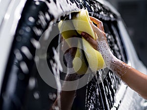 Woman hand with yellow sponge washing car