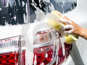 Woman hand with yellow sponge washing car