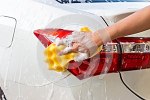 Woman hand with yellow sponge washing taillight modern car or cleaning automobile.