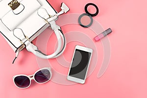 Woman handbag with makeup and accessories isolated on pink background
