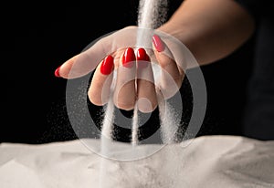 Woman with handful of white dry sand in her hands, spilling sand through fingers on black studio background. Concept of