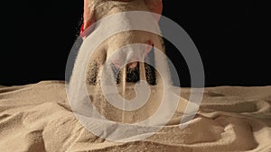 Woman with handful of white dry sand in her hands, spilling sand through her fingers on black studio background. Close