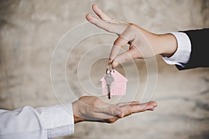 Woman handing over the house keys to a new home inside empty gray colored room