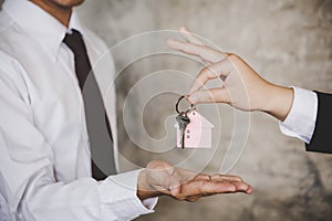 Woman handing over the house keys to a new home inside empty gray colored room