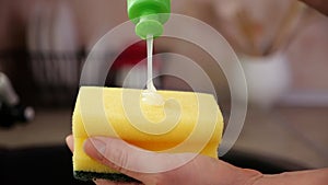 Woman hands apply washing up liquid on sponge from recipient