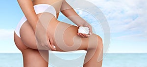Woman hands applying moisturizer cream on thigh, isolated on sea