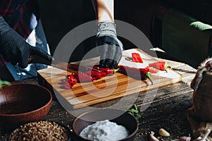 Woman hands in black gloves chopping red hot chili peppers