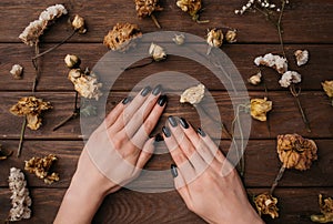 Woman hands with black manicure among dry plants.