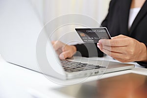 Woman hands in black suit sitting and holding credit card and using laptop computer on table for online payment or shopping online