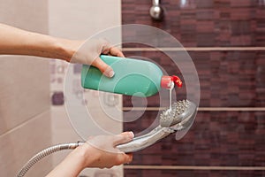 Woman hands with bottle of cleaning detergent for bathroom applies a scour to the metal shower head.
