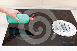 Woman hands with bottle of cleaning detergent for induction stove applies a scour to the burner
