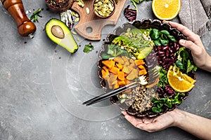 Woman hands with bowl of delicious quinoa salad with avocado, sweet potato, beans on gray background. superfood concept. Healthy,