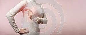 Woman hands checking lumps on her breast for signs of breast cancer on pink background. Healthcare world health day concept