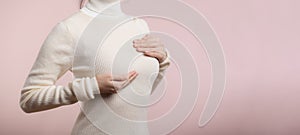 Woman hands checking lumps on her breast for signs of breast cancer on pink background. Healthcare world health day concept