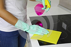 Woman hands cleaning a modern black induction hob by a rag and spray