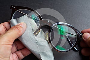 Woman hands cleaning shortsighted or nearsighted eyeglasses by microfibre cleaning cloths, On black background, Optical concept