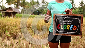 Woman hands with closed sign board on a tropical nature background. Bali island.