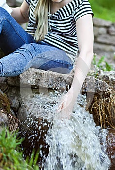 Woman hands in cold water stream in supring park