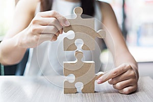 Woman hands connecting couple puzzle over table, businesswoman holding wood jigsaw inside office. Business solutions, mission,