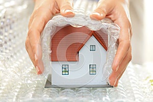 Woman hands covering a model house with bubble wrap- house protection or insurance concept