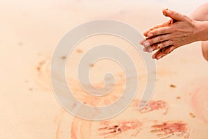 Woman hands creating shapes with red sand on the beach in aboriginal art style