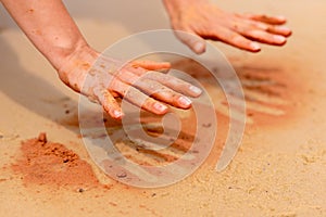 Woman hands creating shapes with red sand on the beach in aboriginal art style