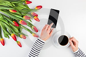 Woman hands with cup of coffee, mobile phone and beautiful flowers bunch on the white office table