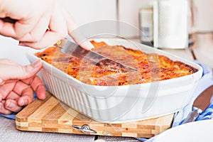 Woman hands cuting meat lasagna in the form of baking. Italian food