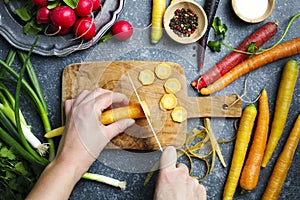 Woman hands cutting carrots on wooden board and fresh spring vegetables for vegetarian cooking on the table