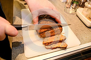 Woman hands cutting piece of meatloaf, she prepare for tasting of food at kitchen. Chef cutting meatloaf with knife on board on
