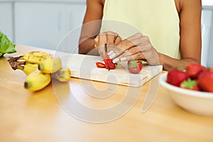 Woman, hands and cutting strawberry in kitchen for diet, healthy meal or fruit salad at home. Closeup of female person