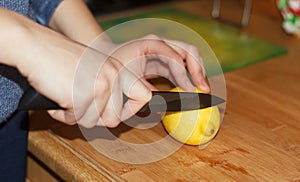 Woman hands cutting a yellow big lemon a kitchen knife