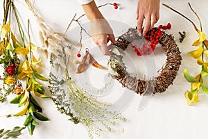 Woman hands with diy floral autumn wreath with driad grass, plant and berry