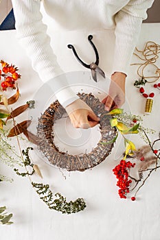 Woman hands with diy floral autumn wreath with driad grass, plant and berry