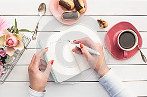 Woman hands drawing or writing with ink pen in open notebook on white wooden table.