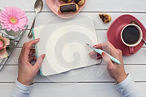 Woman hands drawing or writing with ink pen in open notebook on white wooden table.