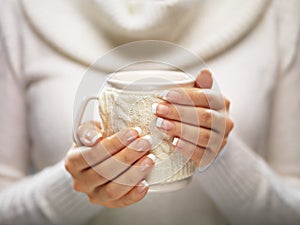 Woman hands with elegant french manicure nails design holding a cozy knitted mug. Winter and Christmas time concept.