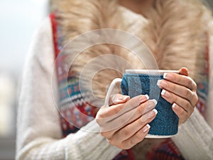 Woman hands with elegant french manicure nails design holding a cozy knitted mug. Winter and Christmas time concept.