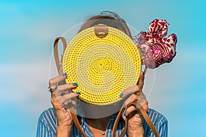 Woman hands with fashionable stylish yellow rattan bag and silk scarf outside. Tropical island of Bali, Indonesia