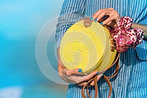 Woman hands with fashionable stylish yellow rattan bag and silk scarf outside. Tropical island of Bali, Indonesia